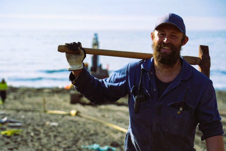 Smilende mann i arbeidsklær med verktøy slengt over ryggen