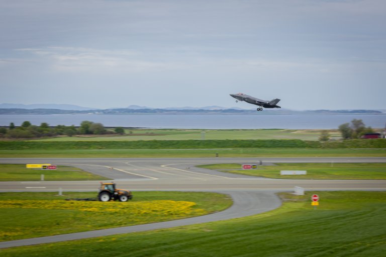 Et norsk F-35 tar av med biodrivstoff (SAF). I forgrunn traktor med arealklipper