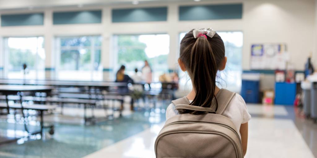 Elementary schoolgirl enters the school cafeteria. She pauses while looking for a friend.